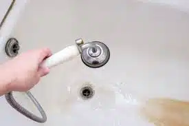 Hand holding showerhead over stained bathtub drain.